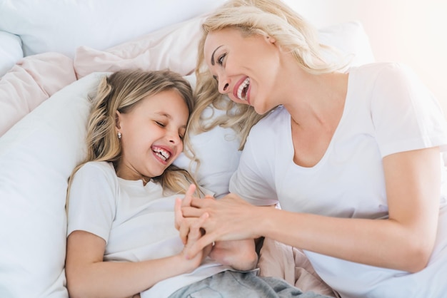 Moeder en haar dochter kind meisje spelen in bed Gelukkig liefdevolle familie concept