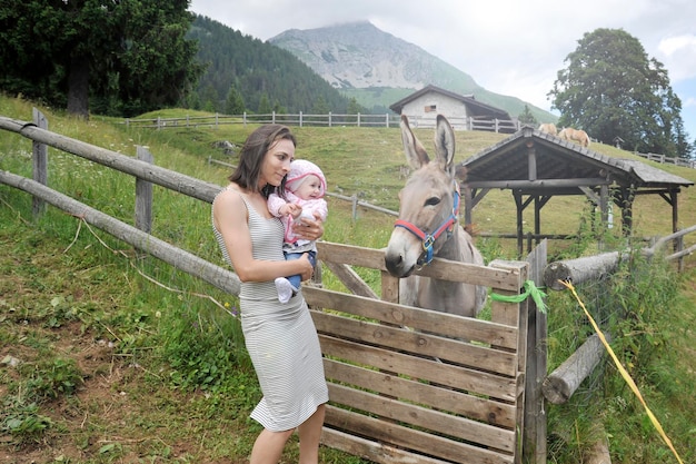 Moeder en haar dochter ontmoeten een ezel op de educatieve boerderij Gelukkig kinderconcept Concept voor huisdiertherapie op het platteland