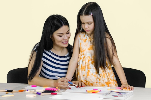 Moeder en haar dochtertje tekenen samen een tafel met potloden en papieren geïsoleerd op pastel