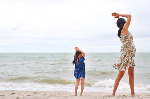 Moeder en haar kind doen yoga-oefeningen op het strand