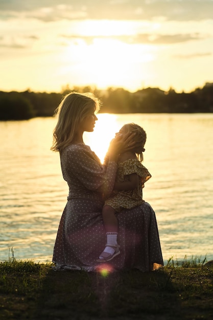 Foto moeder en haar kind knuffelen bij zonsondergang aan het meer belichaamt de rapeutische kracht van de warme tinten van de natuur