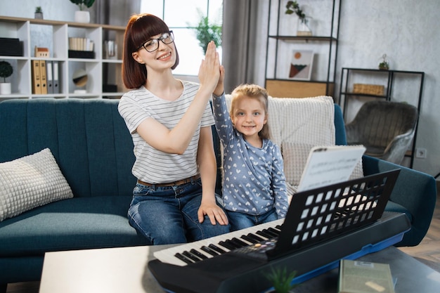 Moeder en haar mooie kleine meisje geven high five na pianospelen in de muziekkamer