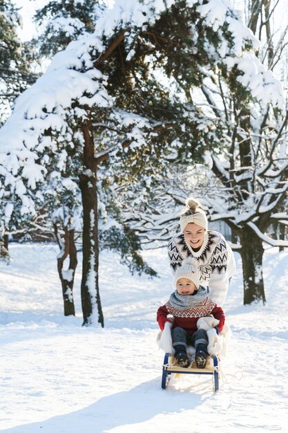 Moeder en haar schattige zoontje dragen warme truien op een sleeheuvel tijdens een zonnige winterdag