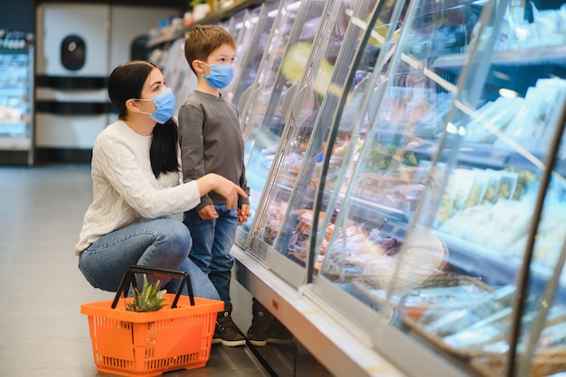 Moeder en haar zoon met beschermend gezichtsmasker winkelen in een supermarkt tijdens de coronavirus-epidemie