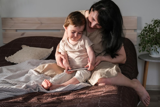 Moeder en haar zoontje zitten op het bed en kijken naar tekenfilms op een smartphone