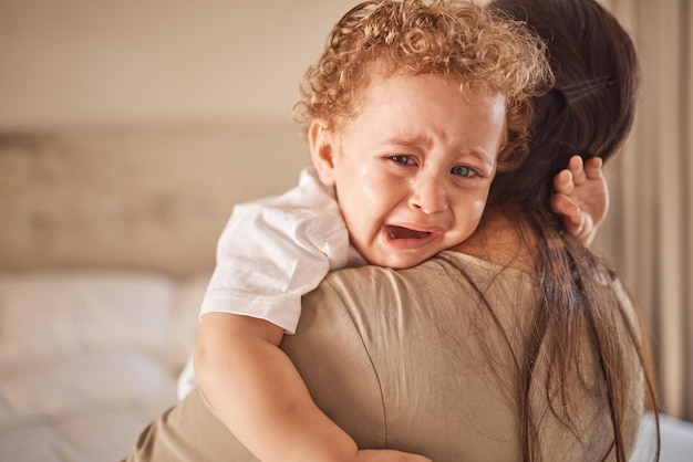 Moeder en huilende baby in een slaapkamer met portret van trieste zoon die boos kijkt tijdens dutje