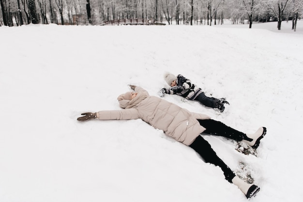 Moeder en jongen liggen met plezier in de sneeuw, actieve levensstijl, winter, familie