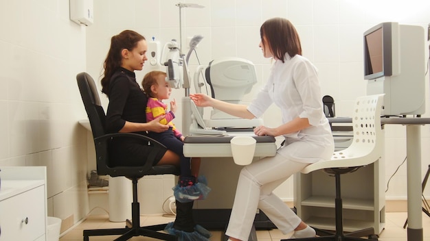 Moeder en kind in de kamer van de oogarts - optometrist in de kliniek die de visie van het kleine kind controleert, horizontaal