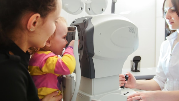 Moeder en kind in oogheelkundige kliniek - optometrist controleert girl's Eye, close-up