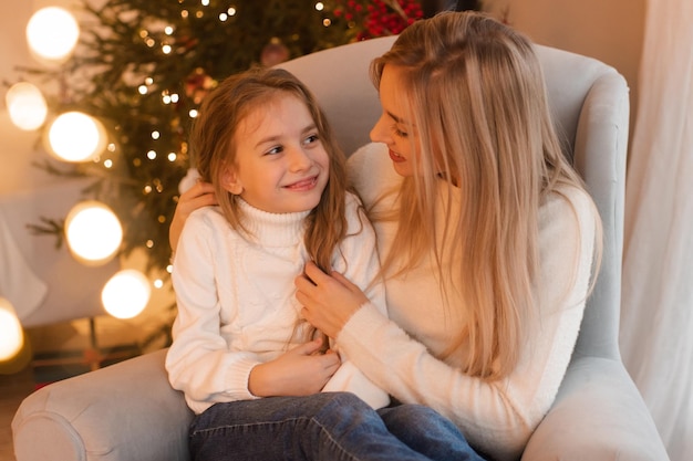 Moeder en kind meisje dochter vieren kerstvakantie zittend in de stoel over kerstboom in de kamer winter groet seizoen viering moederschap