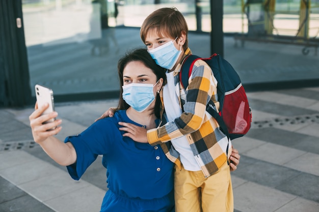 Moeder en kind met een gemaskerde rugzak nemen een selfie aan de telefoon voordat ze naar school of de kleuterschool gaan