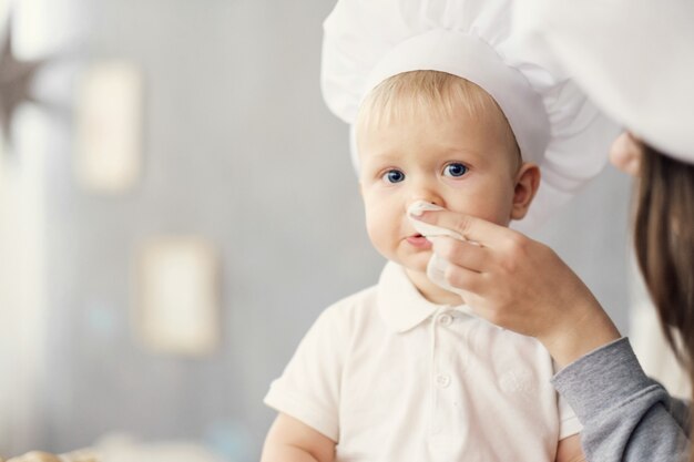 moeder en kind op keuken, witte hoeden van chef, moeder veegt baby af met behulp van servet