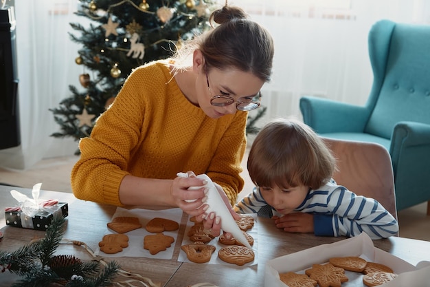 Moeder en kind samen kerstkoekjes versieren met poedersuiker