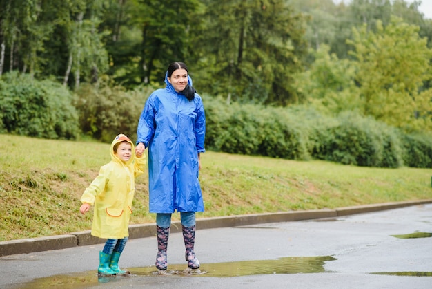 Moeder en kind spelen in de regen, laarzen en regenjassen aan