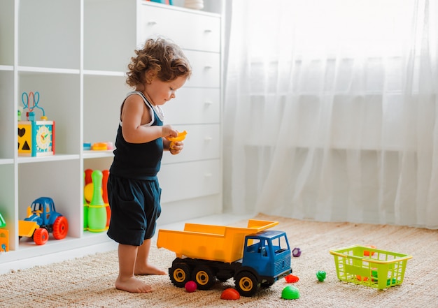 Moeder en kind spelen op de vloer in de kinderkamer. Moeder en kleine babyjongen doen met plastic kleurrijk speelgoed.