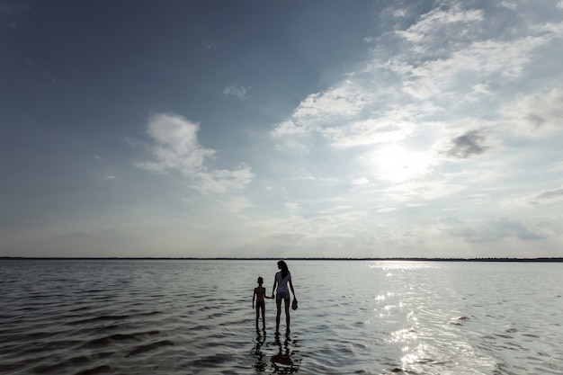 Moeder en kind staan in het water tegen de prachtige zonsondergang op het meer