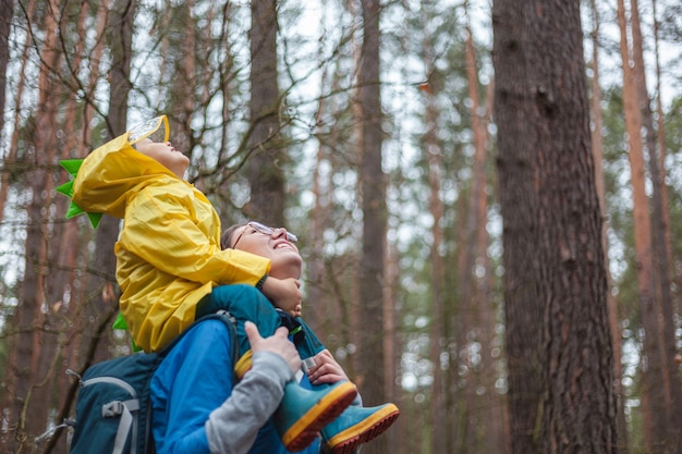 Moeder en kind wandelen samen in het bos na regen in regenjassen