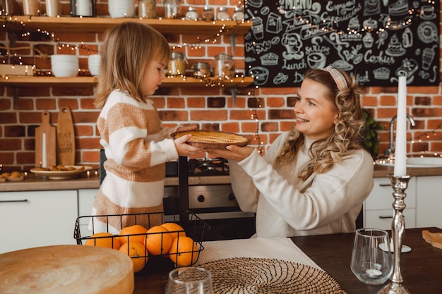 Moeder en kind zitten in de keuken aan tafel met taart en sinaasappels