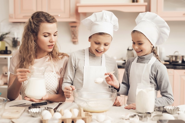 Moeder en kinderen Een deeg maken Gelukkig meisje voegt suiker toe.