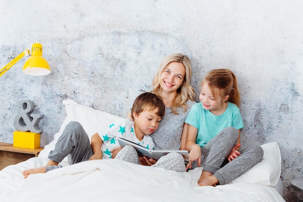Moeder en kinderen lezen thuis een boek op het bed