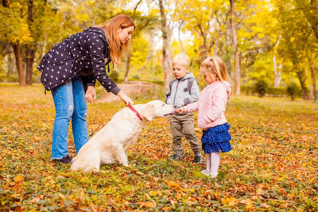 Moeder en kinderen trainen hond in herfstpark. Gelukkige familie op een wandeling met huisdier
