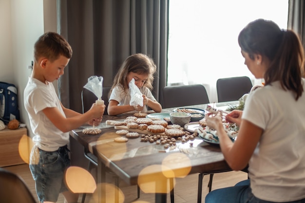 Moeder en kinderen versieren kerst peperkoek thuis een jongen en een meisje schilderen met kornets met su...