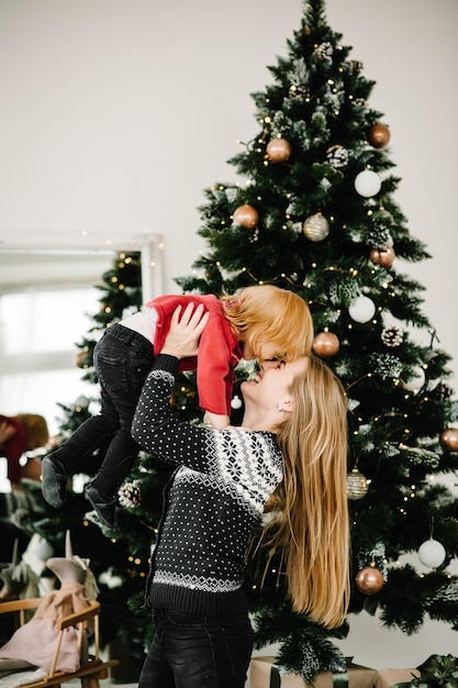 Moeder en klein kind hebben plezier en spelen thuis samen Portret liefdevolle familie close-up Vrolijke moeder knuffelen schattige baby dochter meisje in de buurt van kerstboom Prettige kerstdagen en fijne feestdagen