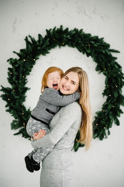 Moeder en klein kind hebben plezier en spelen thuis samen Portret liefdevolle familie close-up Vrolijke moeder knuffelen schattige baby dochter meisje in de buurt van kerstboom Prettige kerstdagen en fijne feestdagen