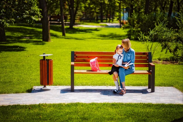 Moeder en kleine dochter in openlucht openbare parkzitting op de bank en het gelezen boek