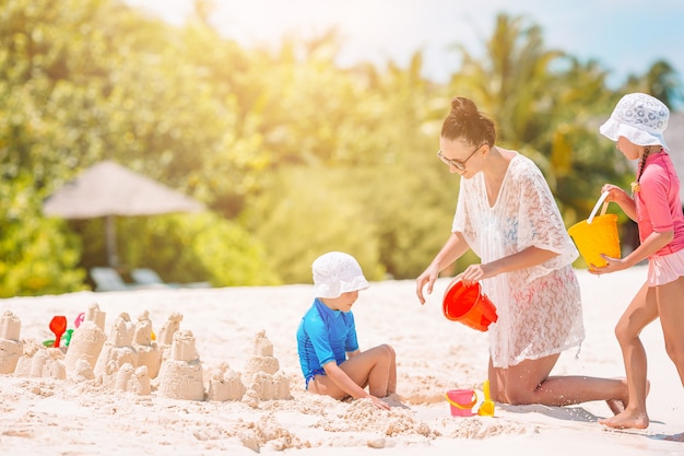 Moeder en kleine dochters die zandkasteel maken bij tropisch strand