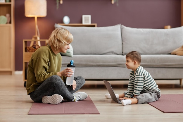 Moeder en kleine jongen met het syndroom van down met behulp van laptop zittend op de vloer thuis