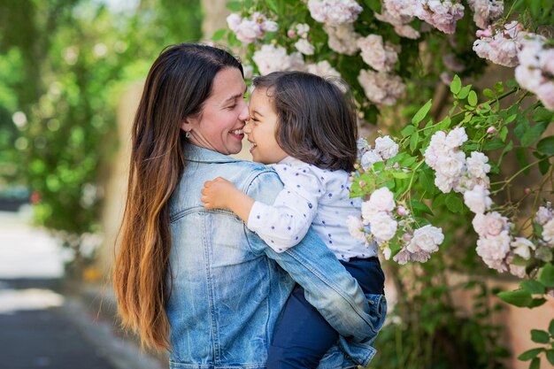 Moeder en kleine knappe babyjongen kijken naar struik met witte rozen