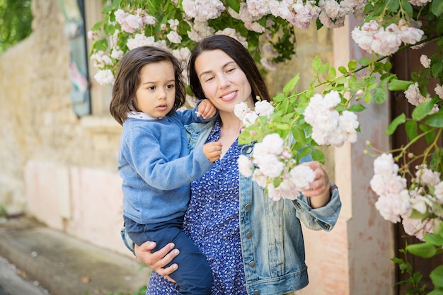 Moeder en kleine knappe babyjongen kijken naar struik met witte rozen