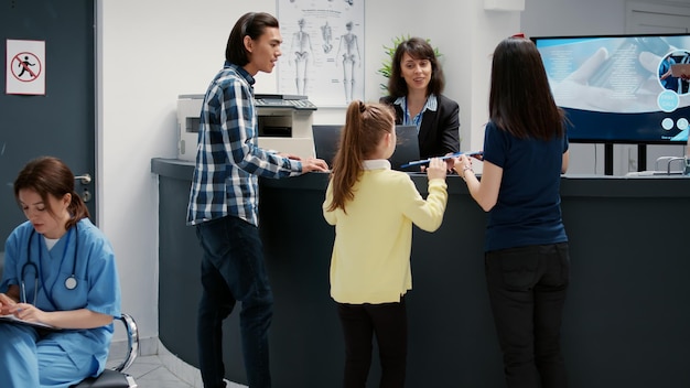 Moeder en meisje schrijven controlerapport bij de receptie van het ziekenhuis om een medische afspraak bij te wonen. Patiënten die een medisch onderzoek ondergaan om ondersteuning en hulp te krijgen.