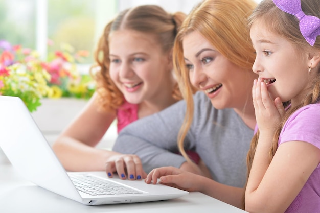 Moeder en meisjes zitten aan tafel en gebruiken laptop