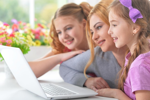 Foto moeder en meisjes zitten aan tafel en gebruiken laptop