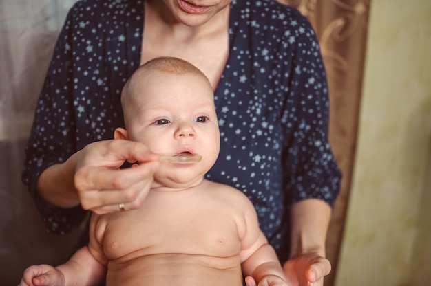 Moeder en pasgeboren grappige emotionele huilende baby naakte babyjongen neemt vloeibare medicatie of