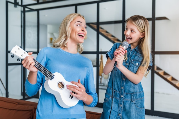 Moeder en schattig klein meisje met microfoon die samen zingen en ukelele spelen