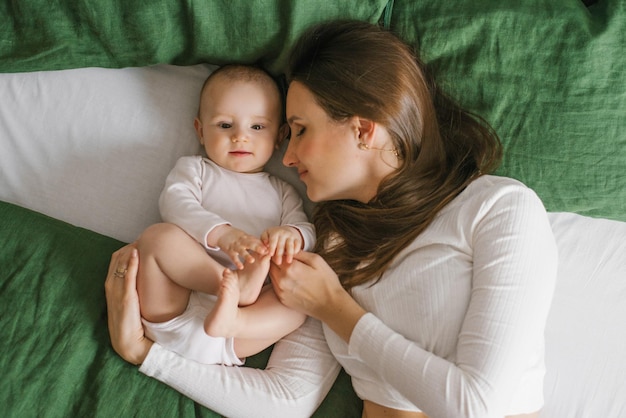 Moeder en schattige baby na het baden liggend op bed thuis