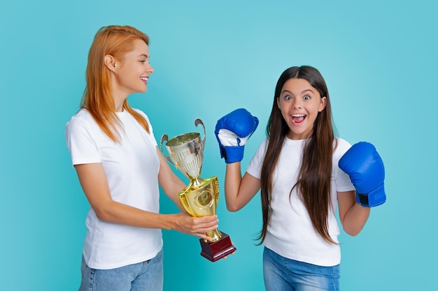 Moeder en tiener kind dochter bedrijf winnende prijs weergegeven: trofee tegen blauwe achtergrond Ouder steun meisje kind vieren overwinning tiener bokser winnaar boksen