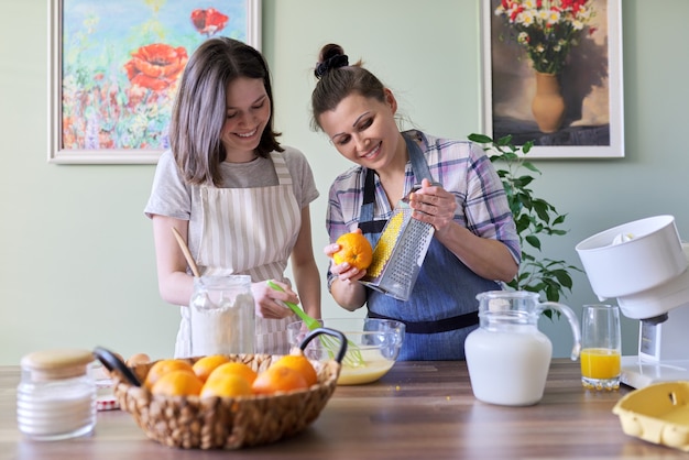 Moeder en tienerdochter koken samen pannenkoeken thuis in de keuken met sinaasappelschil en sap. familie, hobby's, lifestyle, zelfgemaakte lekker en gezond eten