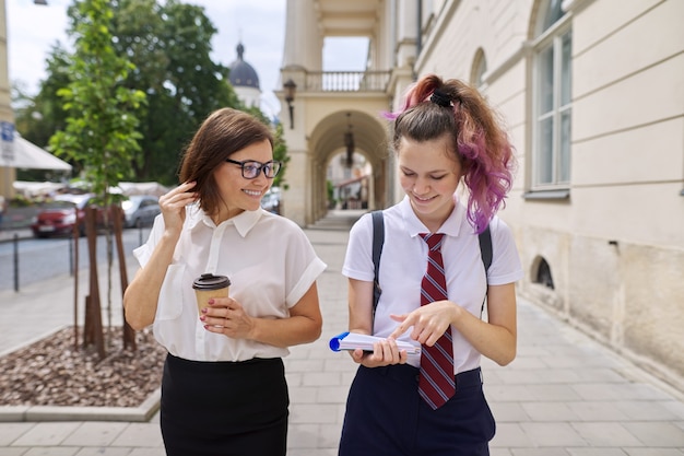 Moeder en tienerdochter lopen samen op straat in de stad. pratende moeder en studente, ouder en kind bespreken school, studie