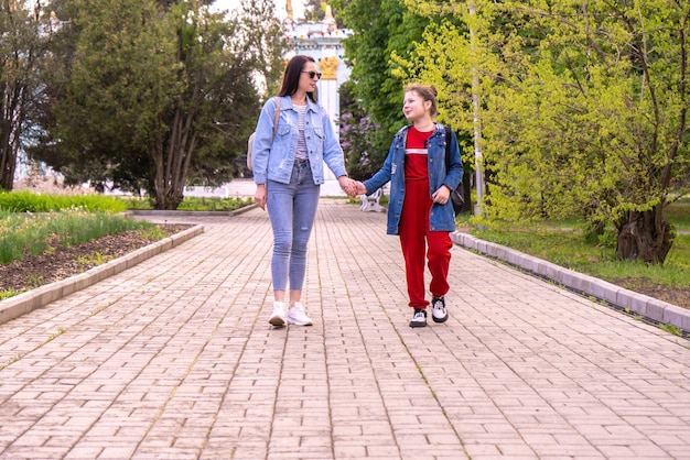 Moeder en tienerdochter wandelen in een park, hand in hand, gelukkige jonge blanke vrouw met lang haar en tienermeisje hangen in een stad, lifestyle-familie