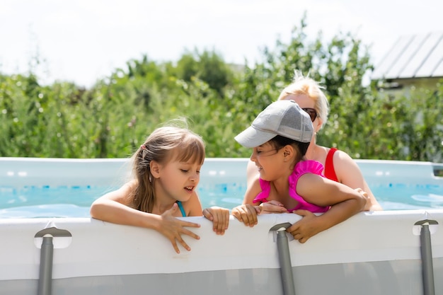 Moeder en twee dochters spelen in zwembadwater. vrouw en twee meisjes hebben plezier in het opspattende water van het huis en glimlachen