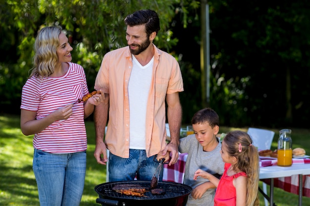 Moeder en vader met kinderen die voedsel koken bij barbecue