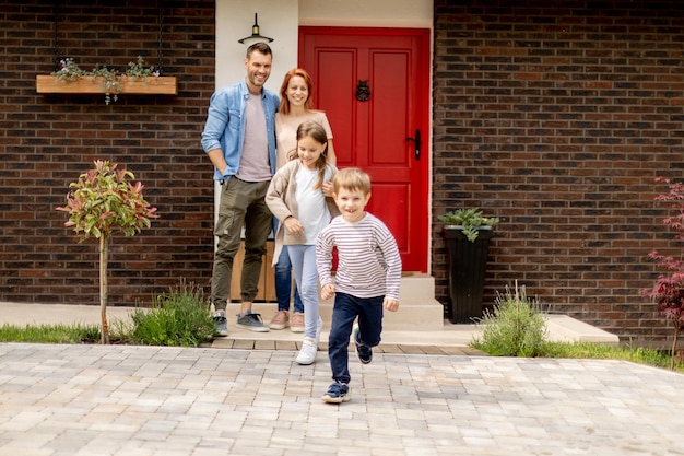 Moeder en vader staan buiten op de veranda van een bakstenen huis terwijl zoon en dochter rennen