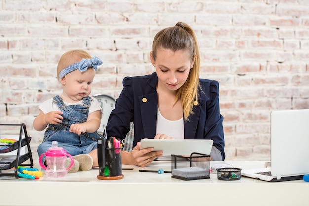 Moeder en zakenvrouw werken met laptopcomputer thuis en spelen met haar babymeisje.