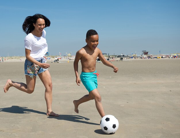 Moeder en zoon die op strand met bal lopen