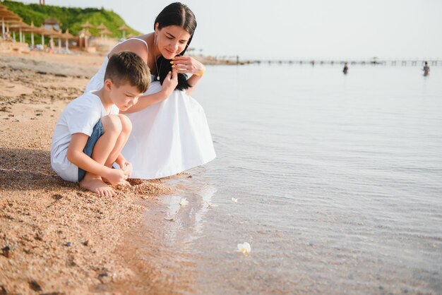 Moeder en zoon die op zonsondergangstrand lopen