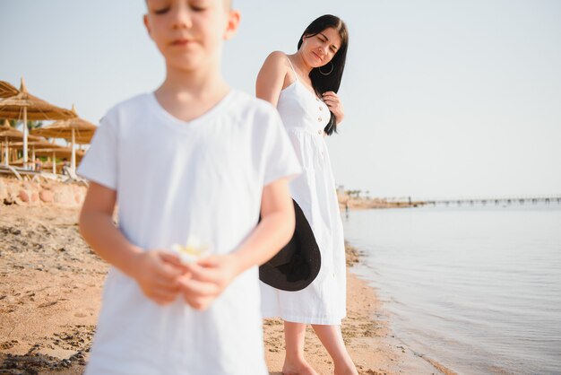 Moeder en zoon die op zonsondergangstrand lopen